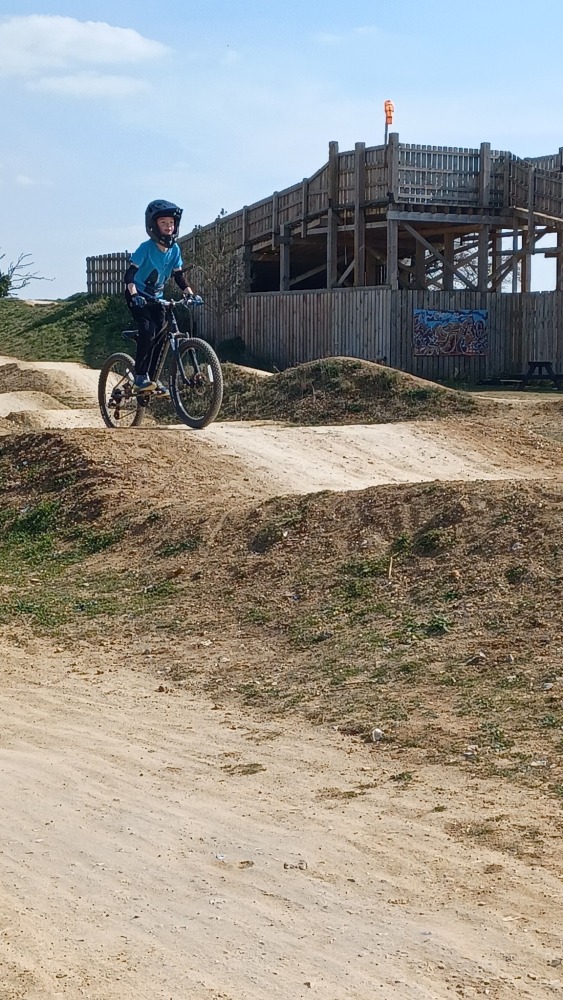 A child wearing a full face helmet, riding their mountain bike over a gravel pump track