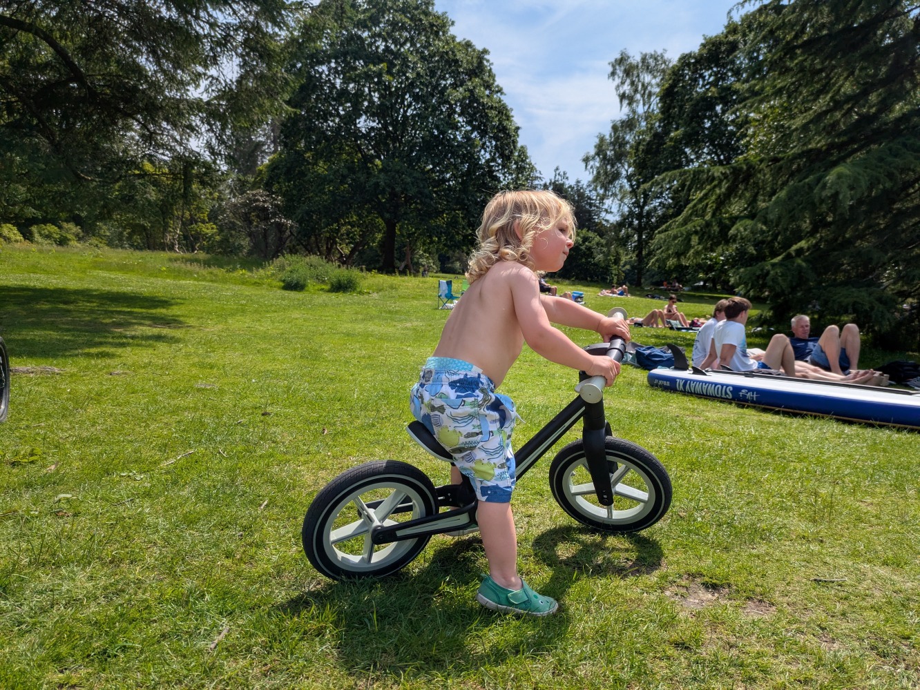 A little boy riding the blue and black Be Fun wheels folding balance bike, on a sunny day by the lake