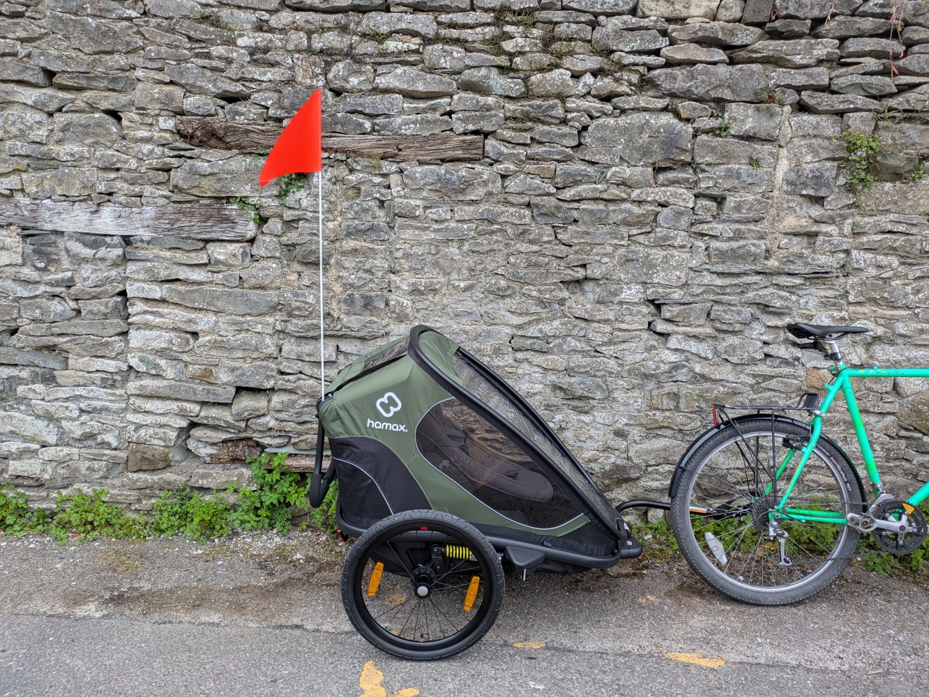 A green Hamax Outback double trailer review- the trailer with an orange flag aginst a wall