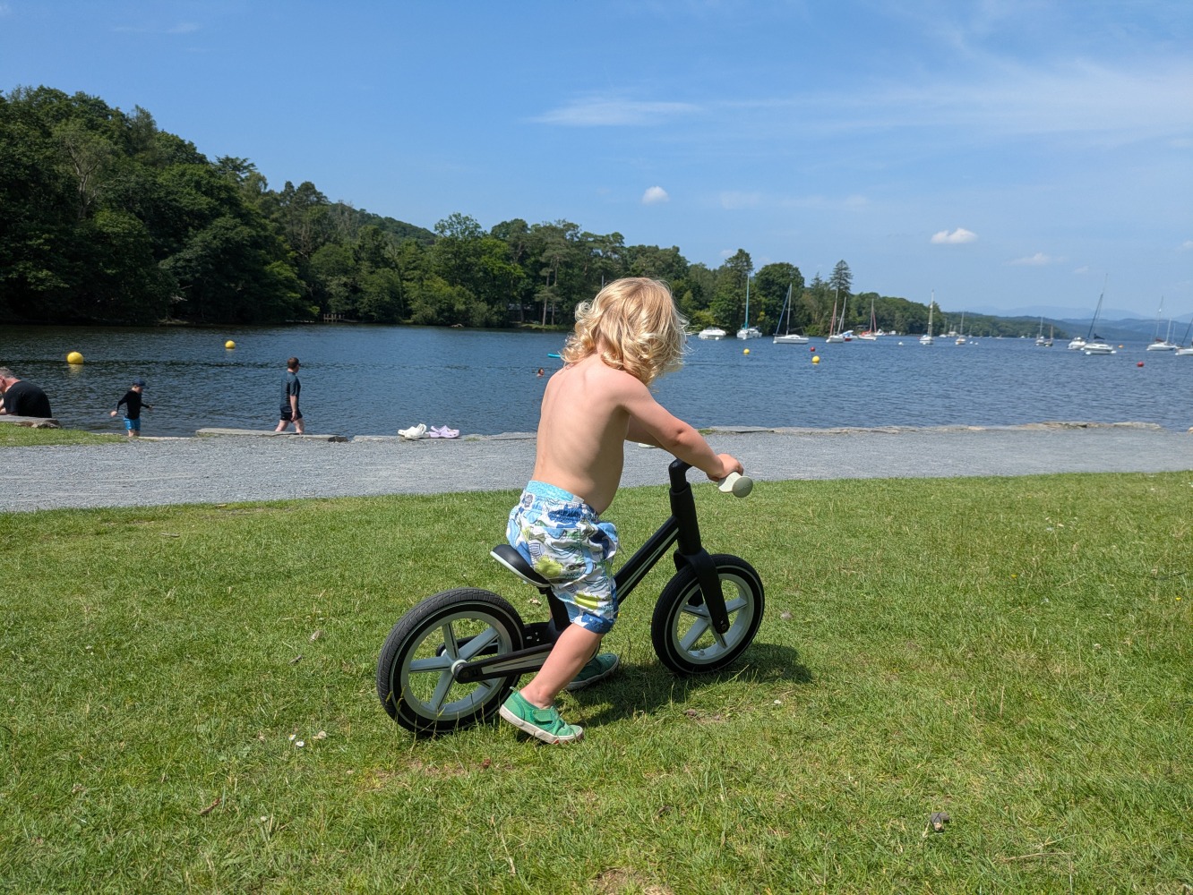 A little boy riding the blue and black Be Fun wheels folding balance bike, on a sunny day by the lake