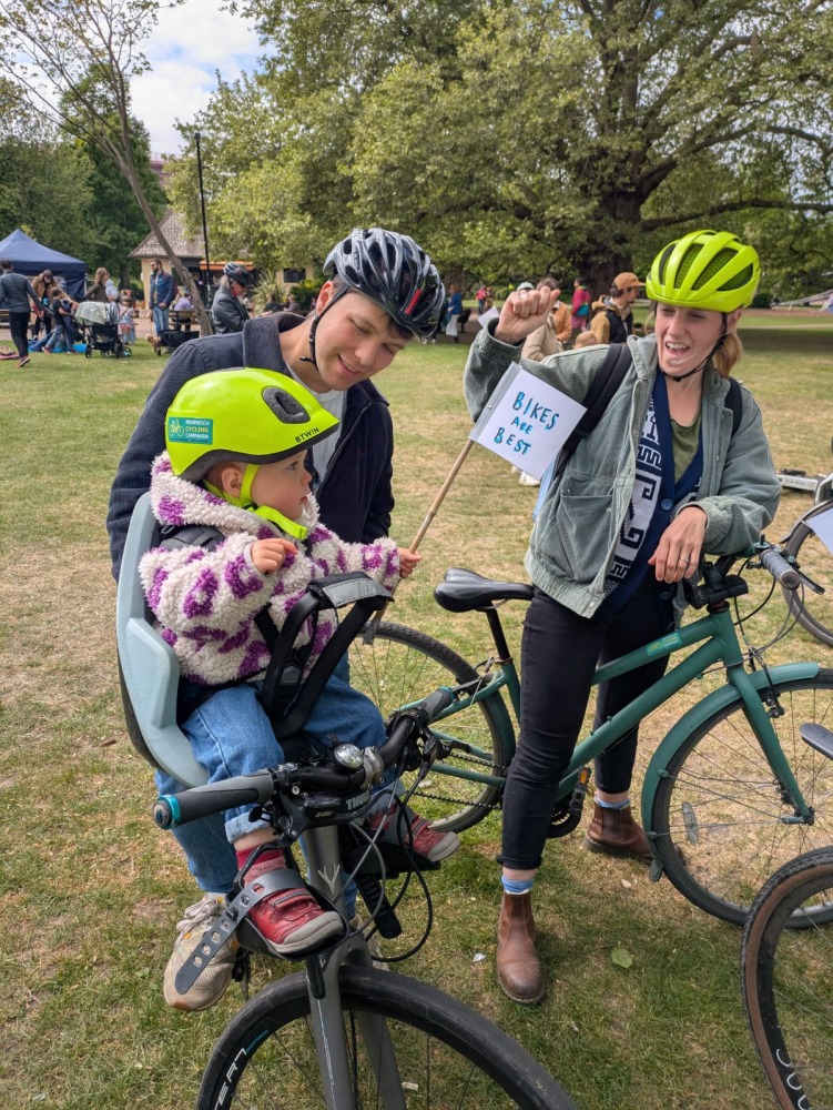 A family on a bike ride, with a little girl on a front bike seat with a 'bikes are best' flag