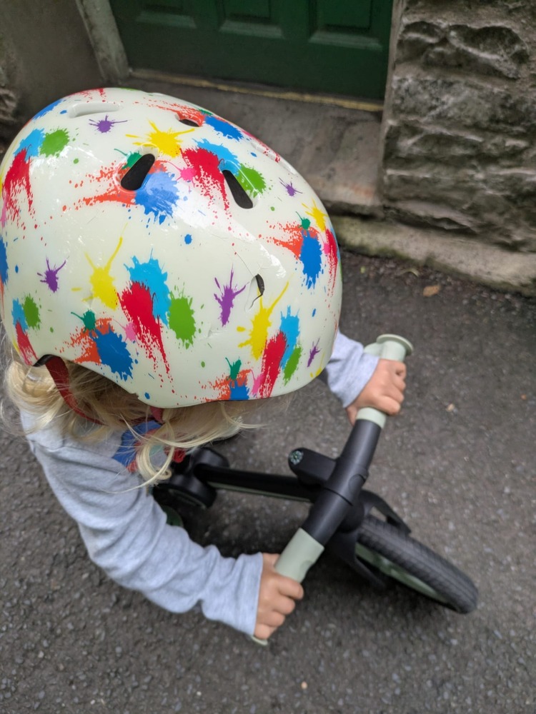 A little boy wearing stripy leggins and a coulourful helmet riding the blue and black Be Fun wheels folding balance bike