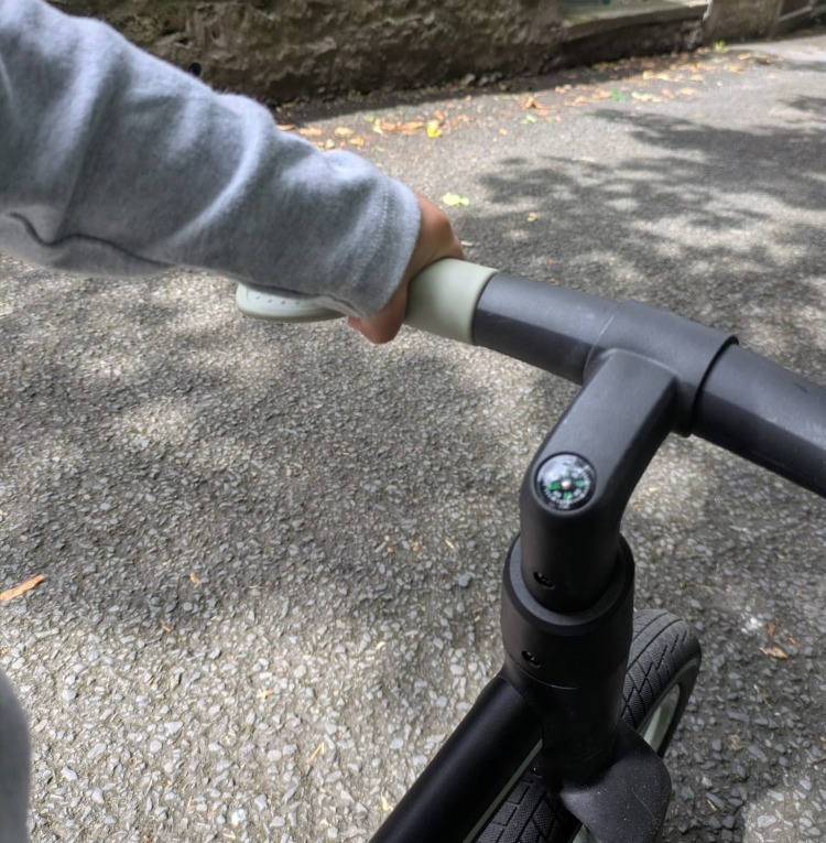 A little boy wearing stripy leggins and a coulourful helmet riding the blue and black Be Fun wheels folding balance bike, showing off the compass on the handlebars