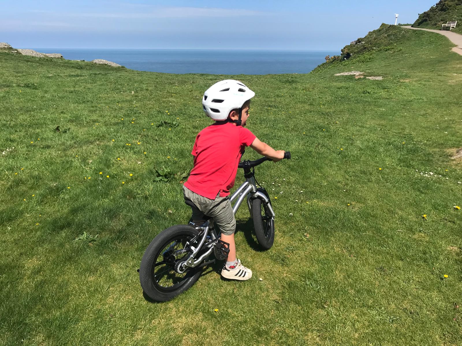 A little boy riding the Early Rider Belter 14 on a sunny day by the sea