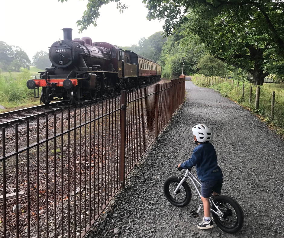 A little boy riding the Early Rider Belter 14 stopped to look at a passing steam train