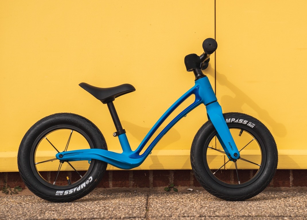 A blue Hornit AIRO 12 balance bike leaning against a yellow wall