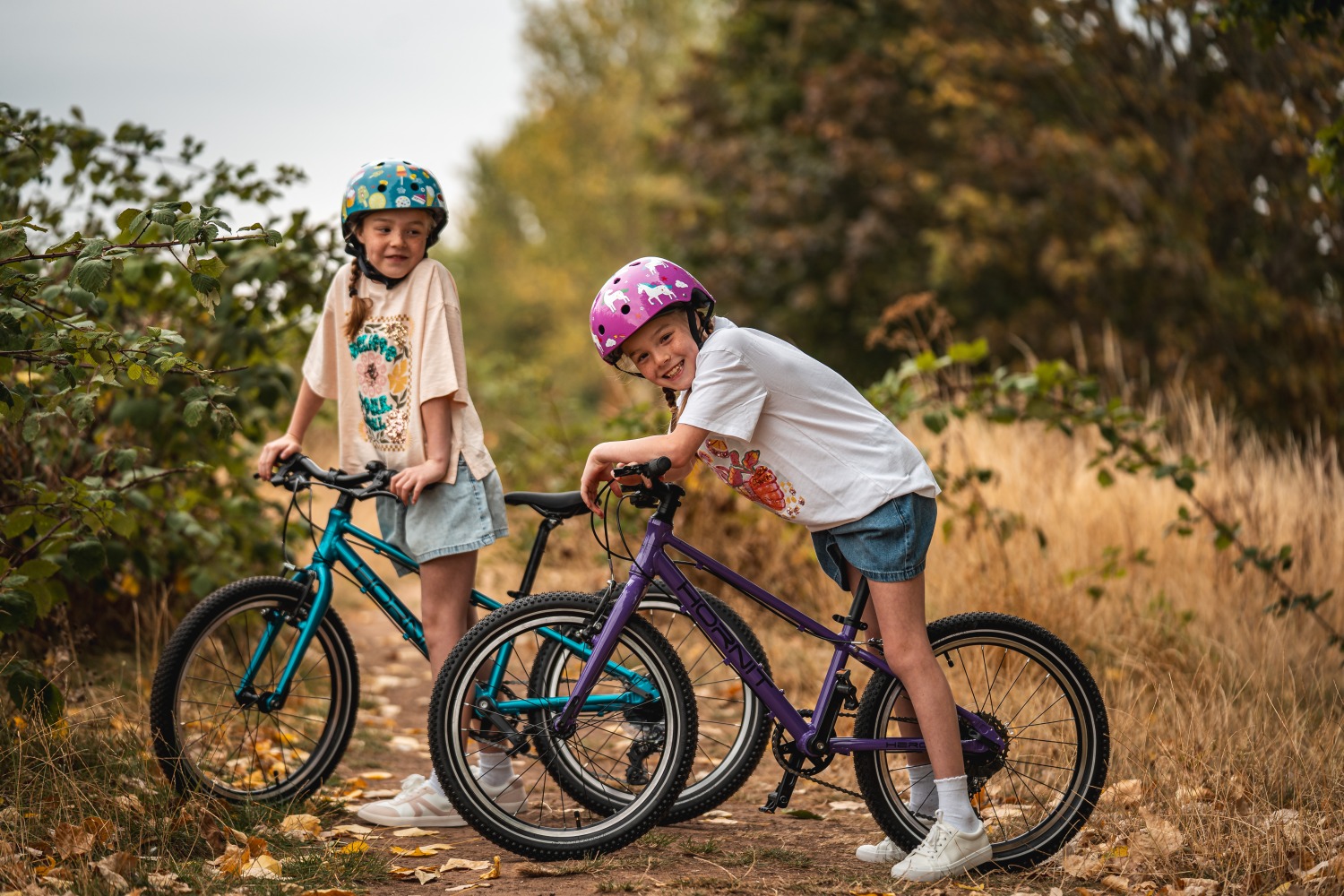 Two little girls standing over hornit bikes with bushes behind them