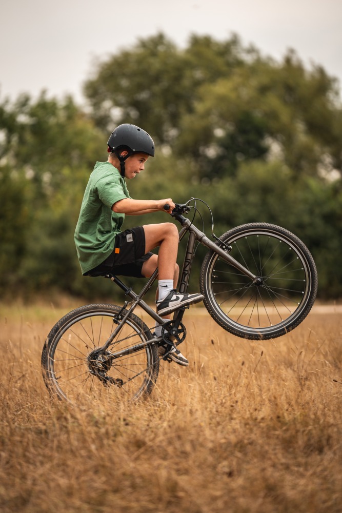 A little boy doing a wheelie in a meadow on a hornit 24 inch bike