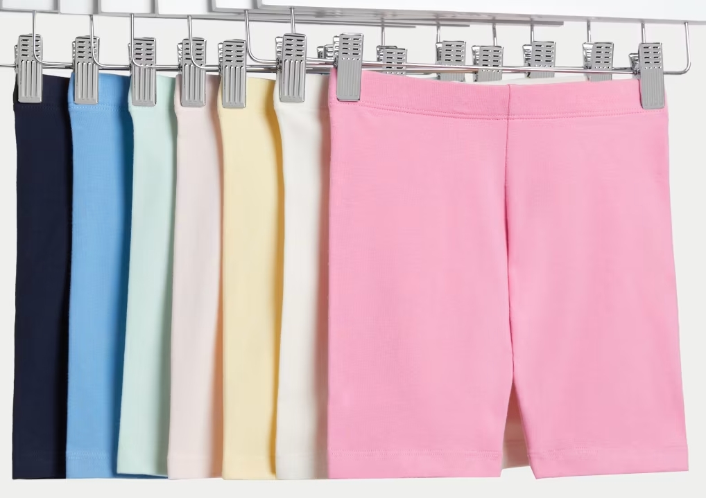 Best kids cycle shorts: A selection of different coloured kids PE shorts hanging from silver hangers