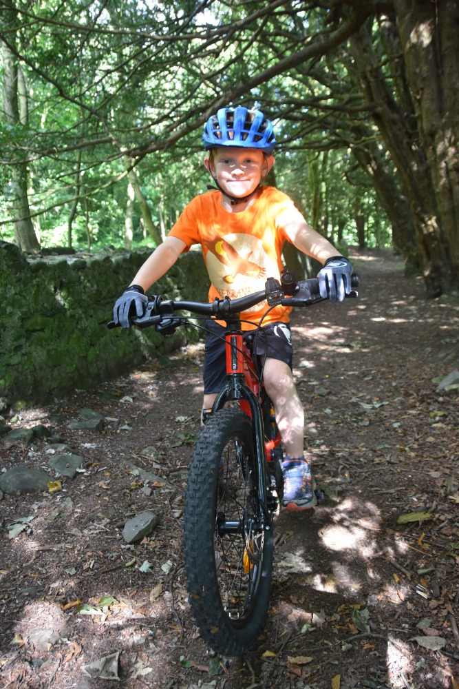 A little boy in an orange top reviewing the Red 20 inch BTWIN EXPL 900r mountain bike
