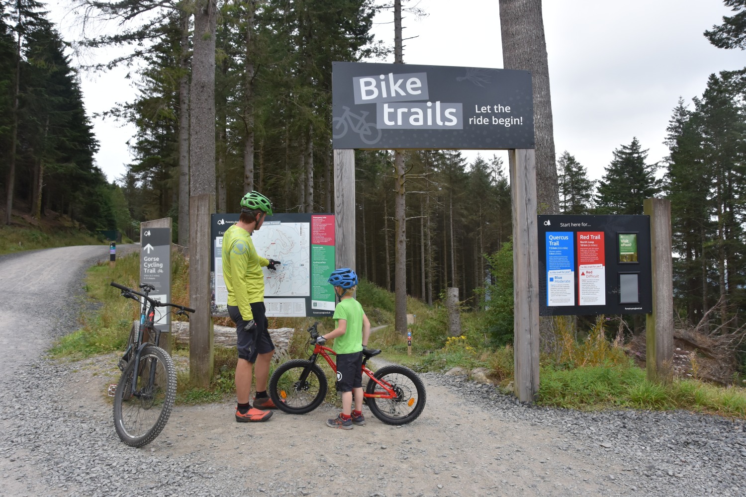 A little boy riding the Red 20 inch BTWIN EXPL 900r mountain bike at a trail centre with his dad.