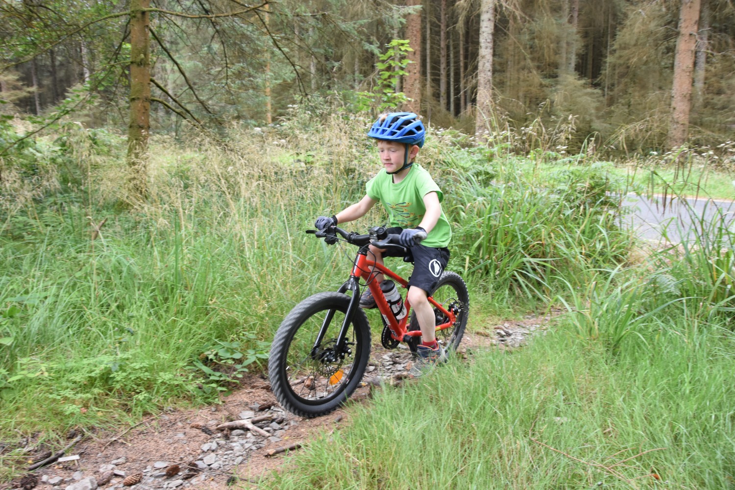 A little boy in an orange top riding the Red 20 inch BTWIN EXPL 900r  kids mountain bike for a review