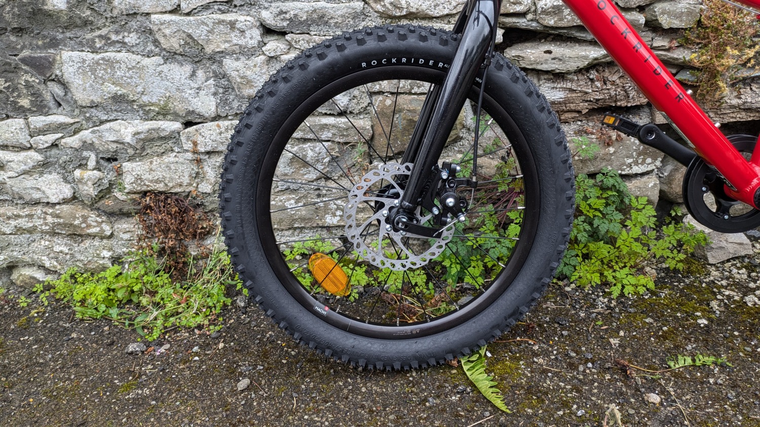 Red 20 inch BTWIN EXPL 900r MTB leant against a wall- close up of the front wheel