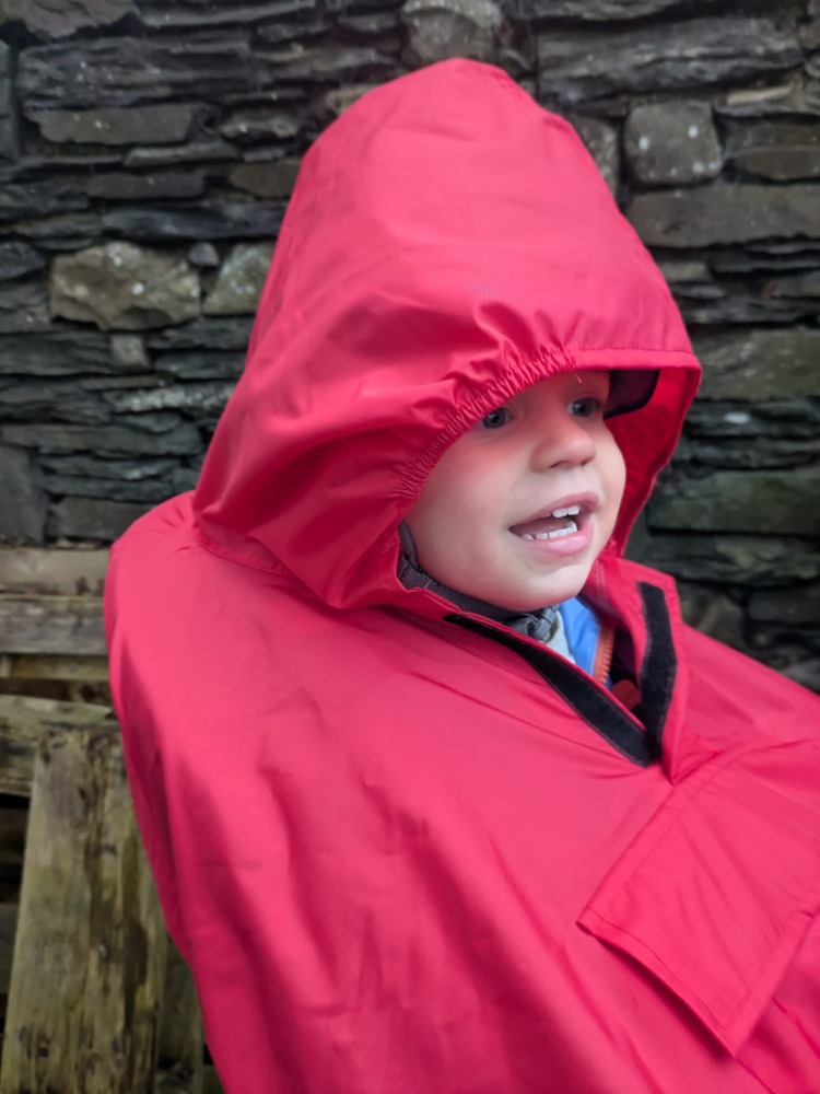 a little boy on a rear bike seat in his red Hamax Bike Seat Rain Poncho