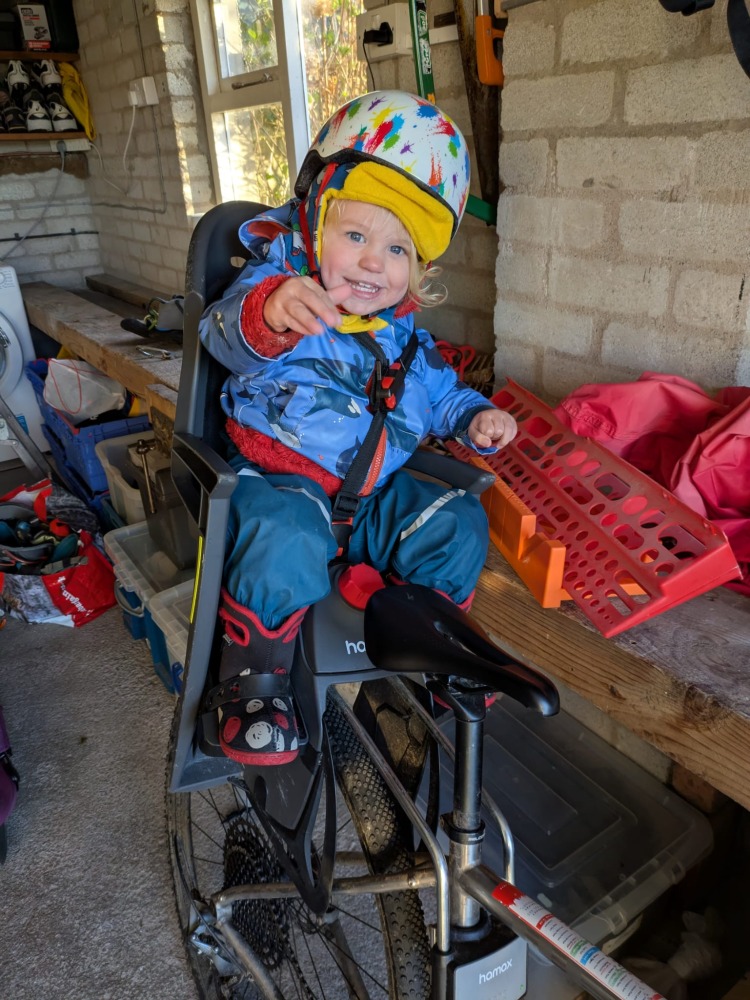 a little boy on a rear bike seat in his red Hamax Bike Seat Rain Poncho