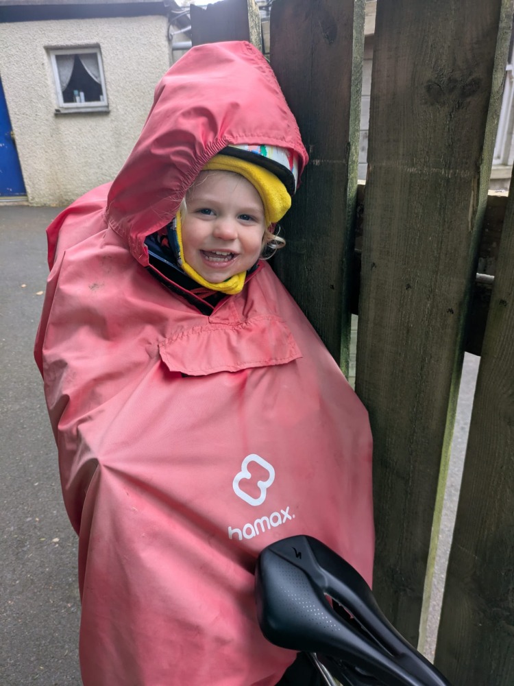 a little boy on a rear bike seat in his red Hamax Bike Seat Rain Poncho