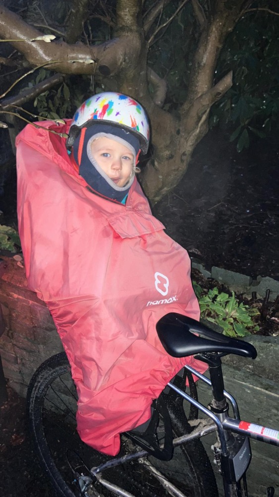 a little boy on a rear bike seat in his red Hamax Bike Seat Rain Poncho